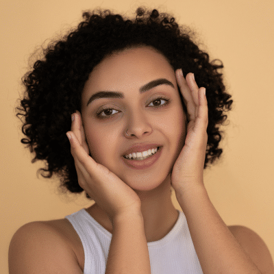 Woman smiling, holding her face, representing facial aesthetics in cosmetic dentistry